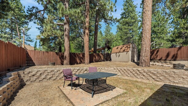 Un jardin avec une table et des chaises de patio, entouré d’une clôture en bois et d’arbres.