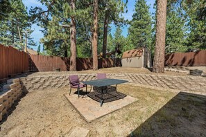 A backyard with a patio table and chairs, surrounded by a wooden fence and trees. - Chipmunk House (Big Bear Lake)