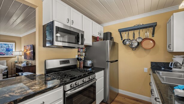 A modern kitchen with white cabinetry, stainless steel appliances, and a wooden floor. - Chipmunk House (Big Bear Lake)