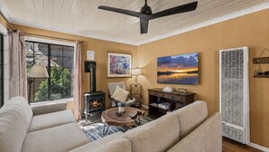 Un salon avec un canapé, une cheminée, un ventilateur de plafond, un tableau et une fenêtre avec des rideaux.