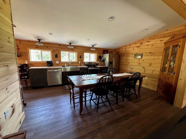Una cocina tipo cabaña con una mesa y sillas, paredes de madera y un refrigerador.