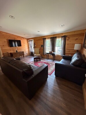 Una habitación con paneles de madera, un sofá, una silla, una mesita y un televisor montado en la pared.