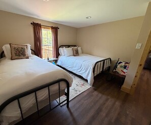 A bedroom with two beds, a window with curtains, and a wooden floor. - Cabin Fever II is a cozy 3-bedroom cabin in the foothills of the Blue Ridge.  (Luray)
