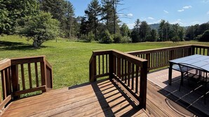 A wooden deck with a table and chairs, surrounded by a grassy field and trees. - Cabin Fever II is a cozy 3-bedroom cabin in the foothills of the Blue Ridge.  (Luray)