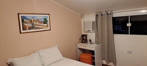A bedroom with a bed, a desk with a chair, a window with curtains, and a wall-mounted air conditioner.