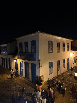 A historic building with multiple blue doors and windows, a cobblestone street, and a group of people gathered in front.