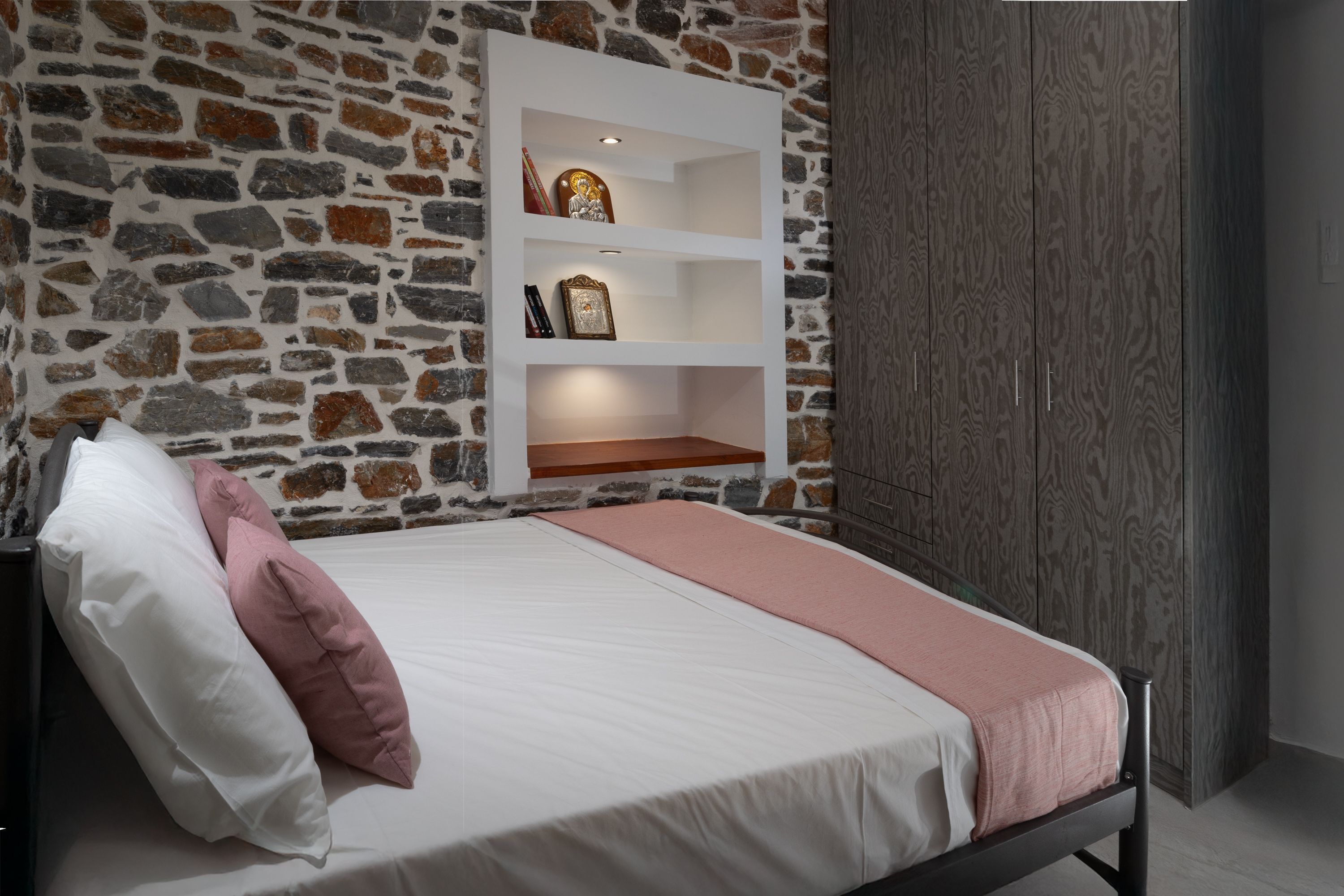 A bed with white and pink bedding, a stone wall, and a wooden wardrobe.