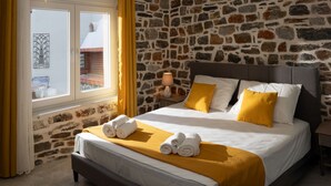 Ein Schlafzimmer mit einer Steinwand, einem Bett mit weißer und gelber Bettwäsche sowie einem Fenster mit Vorhängen.