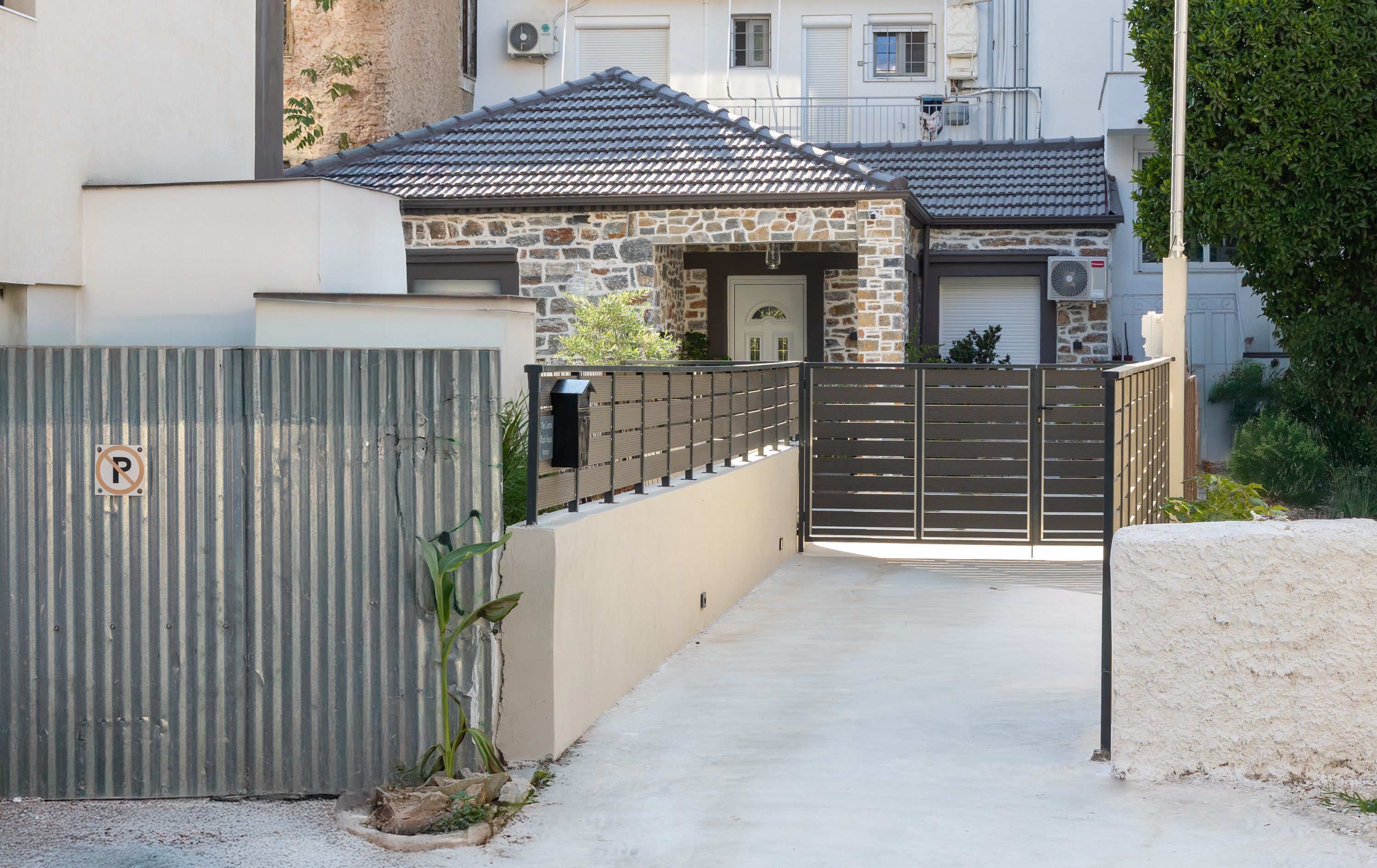 A gated residential area with a stone house, a metal gate, and a concrete pathway.