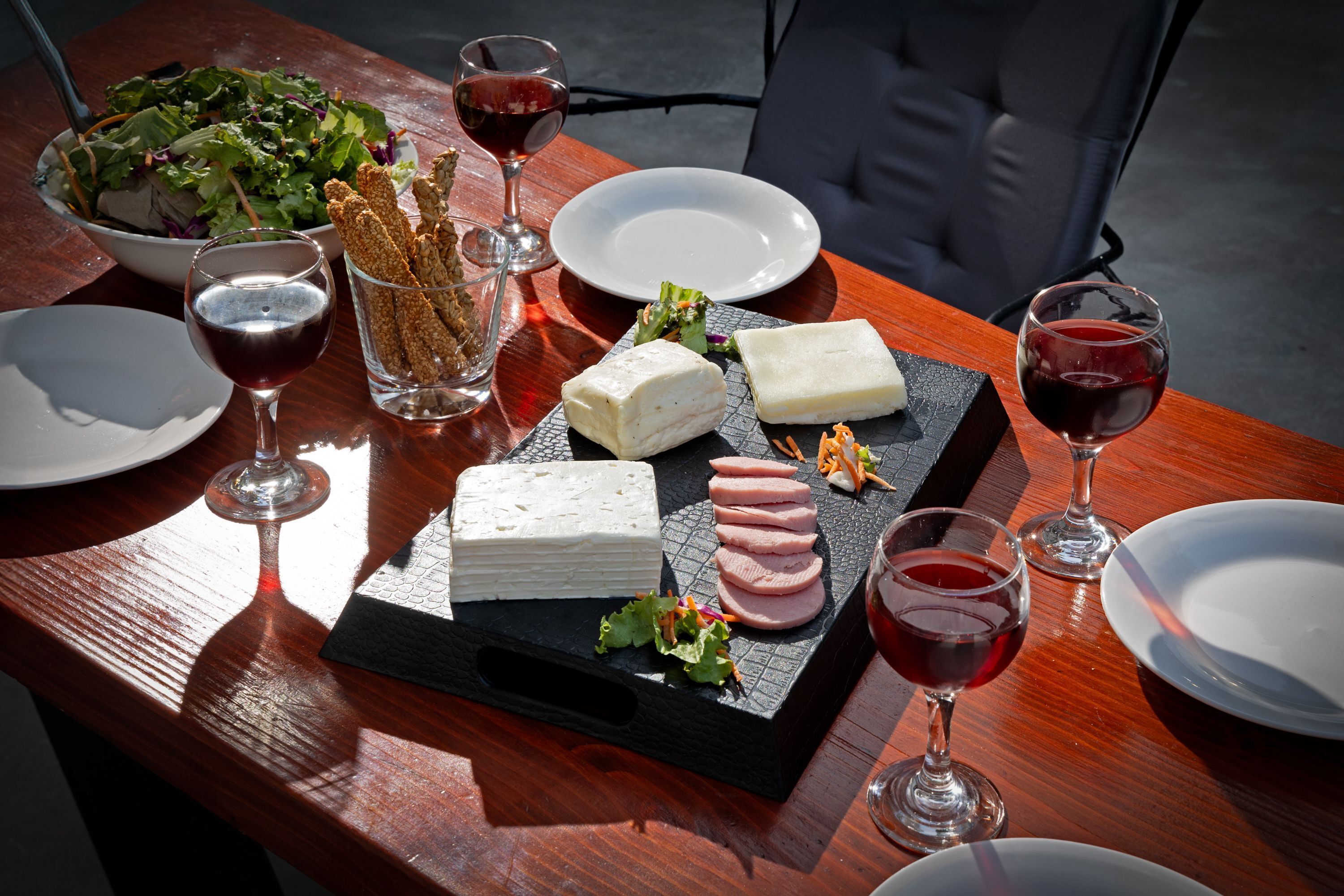 Een houten tafel met een kaasplank, salade en wijnglazen.