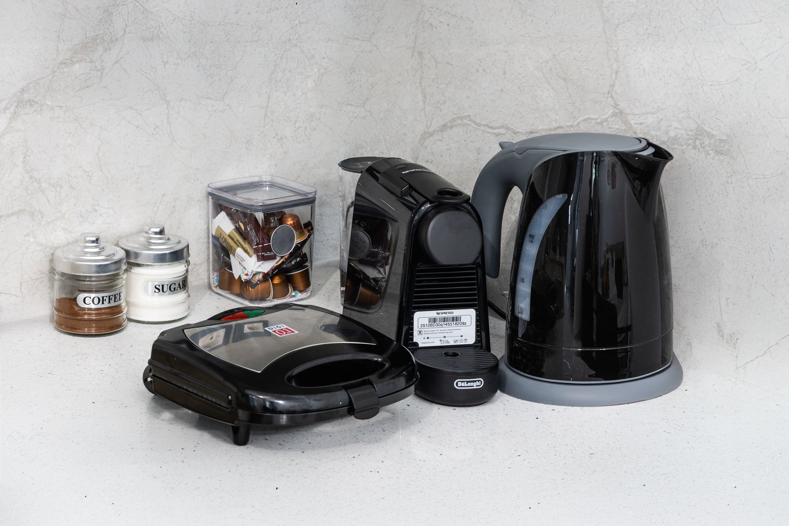 A coffee maker, a kettle, a jar labeled 'SUGAR', and a jar labeled 'COFFEE'.