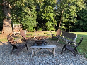A picnic area with benches and a fire pit surrounded by gravel, set in a wooded park.