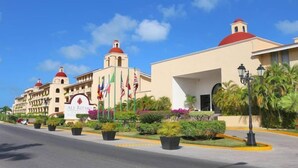 Un hotel con una cúpula roja y fachada color beige, banderas y jardines bien cuidados.