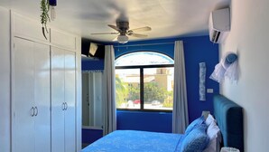 Un dormitorio con una cama, ventilador de techo, ventana con cortinas, armario y aire acondicionado.