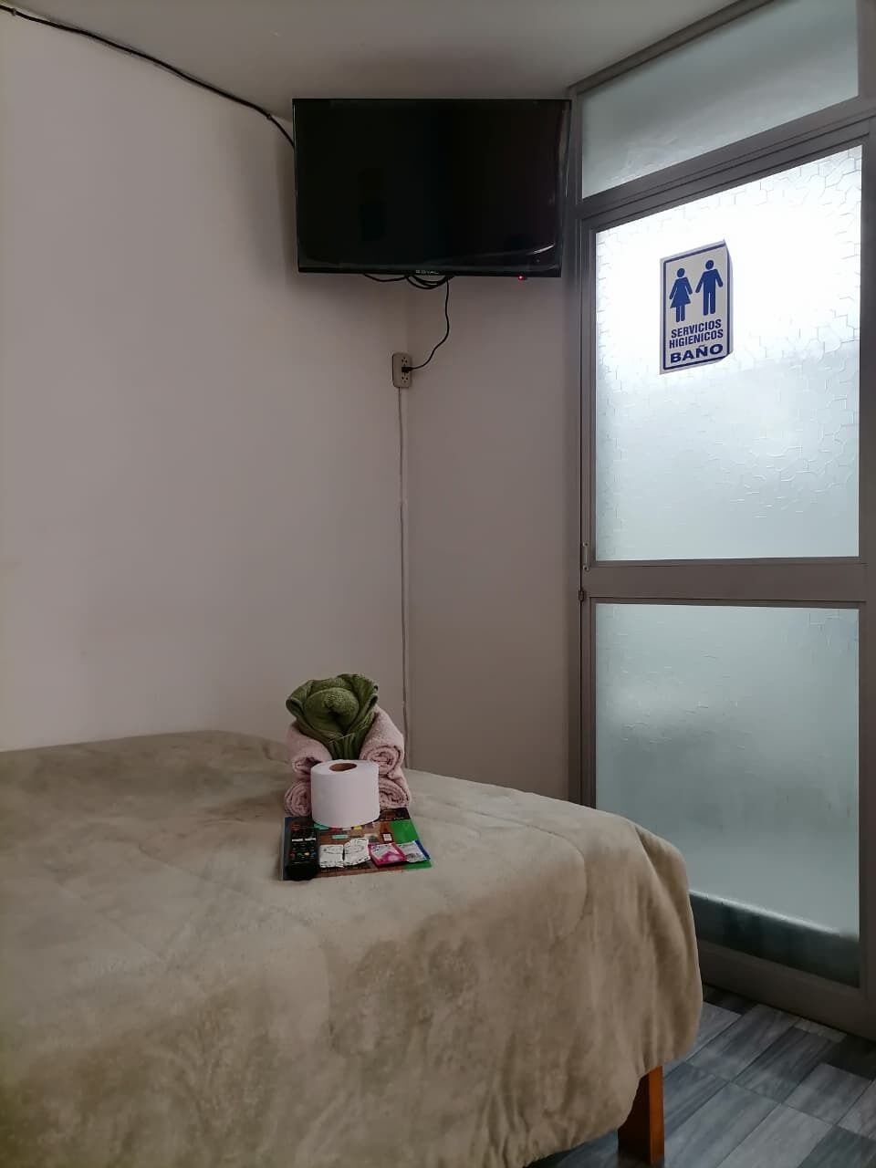 Een kamer met een bed, een aan de muur bevestigde televisie, een raam met een geëtste glasdecoratie, en een bordje met de aanduiding voor herentoilet.