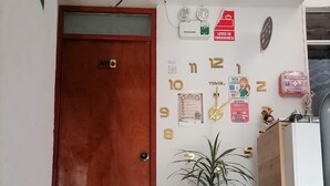 A hotel entrance with a wooden door, a doormat with 'BIENVENIDO' text, a wall clock, emergency signs, and a potted plant. - hostal kactus (Caraz)