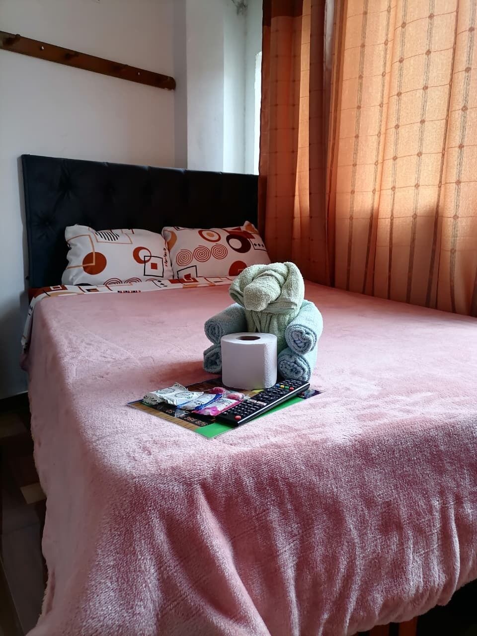 Una cama con un edredón rosa, un osito de peluche, un control remoto y una revista.