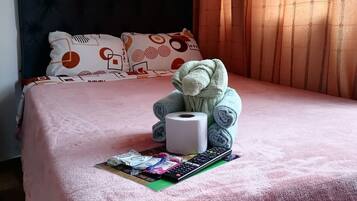 Una cama con un edredón rosa, un osito de peluche, un control remoto y una revista.