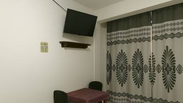 A small room with a TV mounted on the wall, a table with a patterned tablecloth, and a curtain with a geometric design.