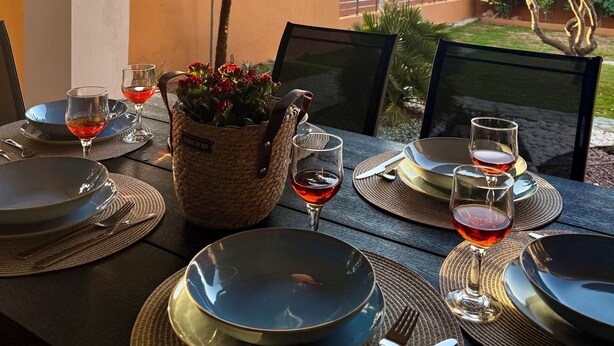 Un área de comedor al aire libre con vistas al mar, mesas dispuestas con platos, cubiertos y copas de vino tinto.
