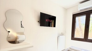 Un dormitorio moderno con una cama, un televisor montado en la pared, un espejo redondo y una ventana con vistas.
