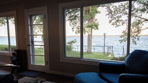 A room with a large window overlooking a body of water, a blue chair, and a wooden table. - Relax by the Waterfront at The Alvig House on
Green Lake (Spicer)