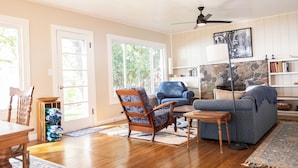 A living room with a wooden floor, a blue sofa, a wooden chair, a dining table, and a stone fireplace. - Relax by the Waterfront at The Alvig House on
Green Lake (Spicer)