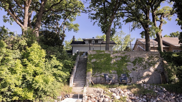A house with a stone staircase leading up to a deck, surrounded by trees and a rocky shoreline. - Relax by the Waterfront at The Alvig House on
Green Lake (Spicer)