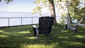 A park bench and a chair facing a body of water, with a tree and a fence in the background. - Relax by the Waterfront at The Alvig House on
Green Lake (Spicer)