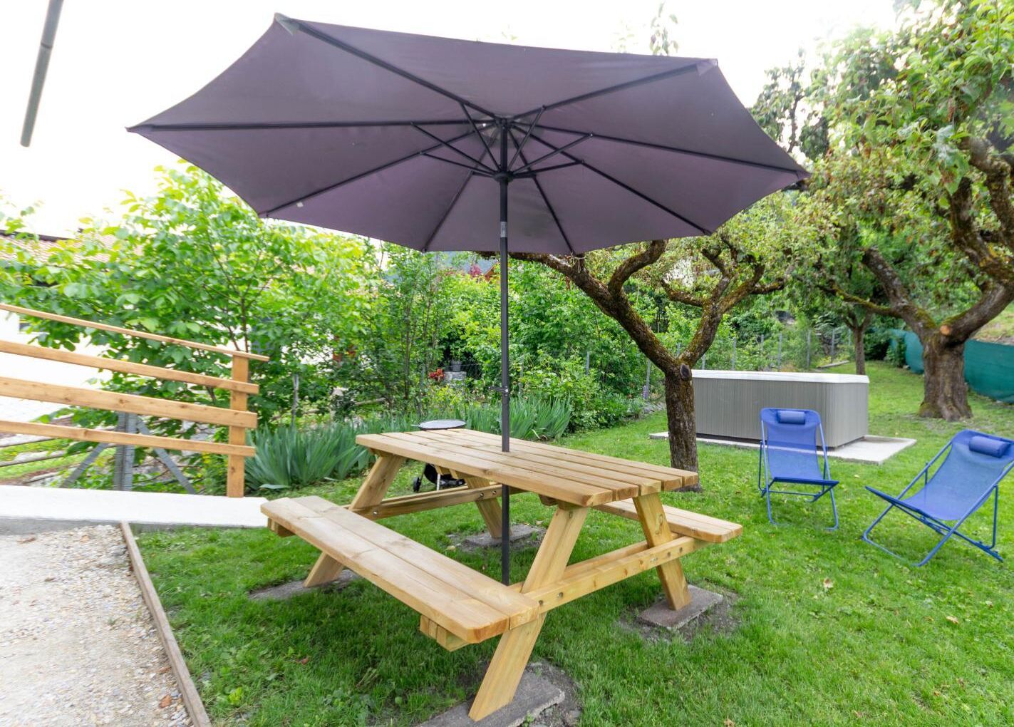 Una mesa de picnic de madera con bancos y un paraguas grande en un jardín.