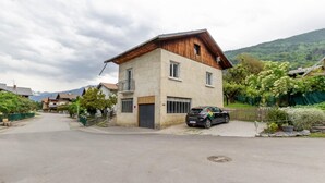 A two-story house with a wooden roof and a balcony, surrounded by greenery and a mountain backdrop. - MUTCHOS - LA PLAGNE TARENTAISE (LA PLAGNE TARENTAISE)