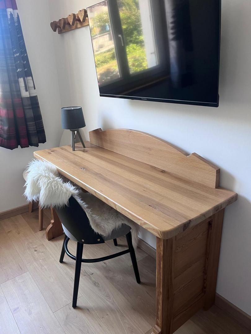 Un bureau en bois, recouvert d’un plaid en fourrure, une chaise, une lampe et un téléviseur fixé au mur.