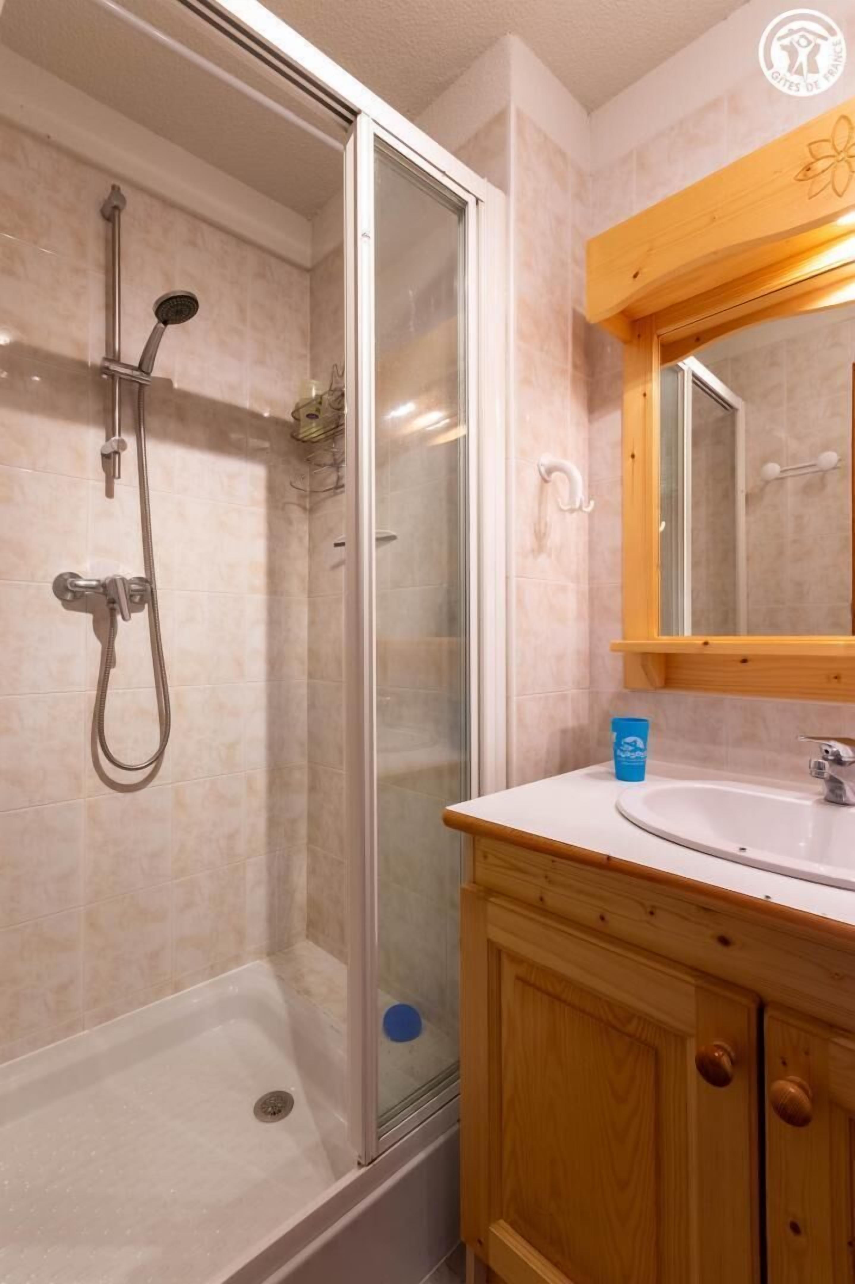 A bathroom with a glass-enclosed shower, a wooden vanity with a sink, and a mirror above the vanity.