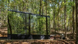 Een bebost gebied met een zwarte metalen constructie, mogelijk een uitkijkpunt, omringd door bomen en een picknickplek met stoelen en een barbecue.