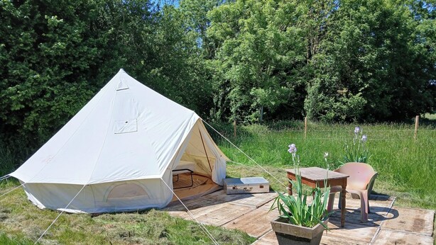 A tent set up in a grassy area with a picnic table and chairs nearby. - "Sur les prés" is a tent set up in a meadow, 100% natural. (Ohey)