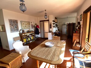 Amplia sala de estar con una mesa de comedor de madera, una estantería y una cocina al fondo.
