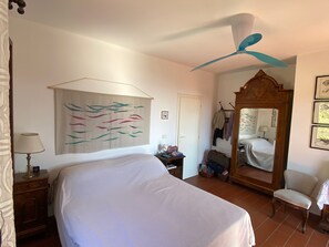 A bedroom with a bed, a ceiling fan, a large mirror, and a wall with a colorful abstract painting.