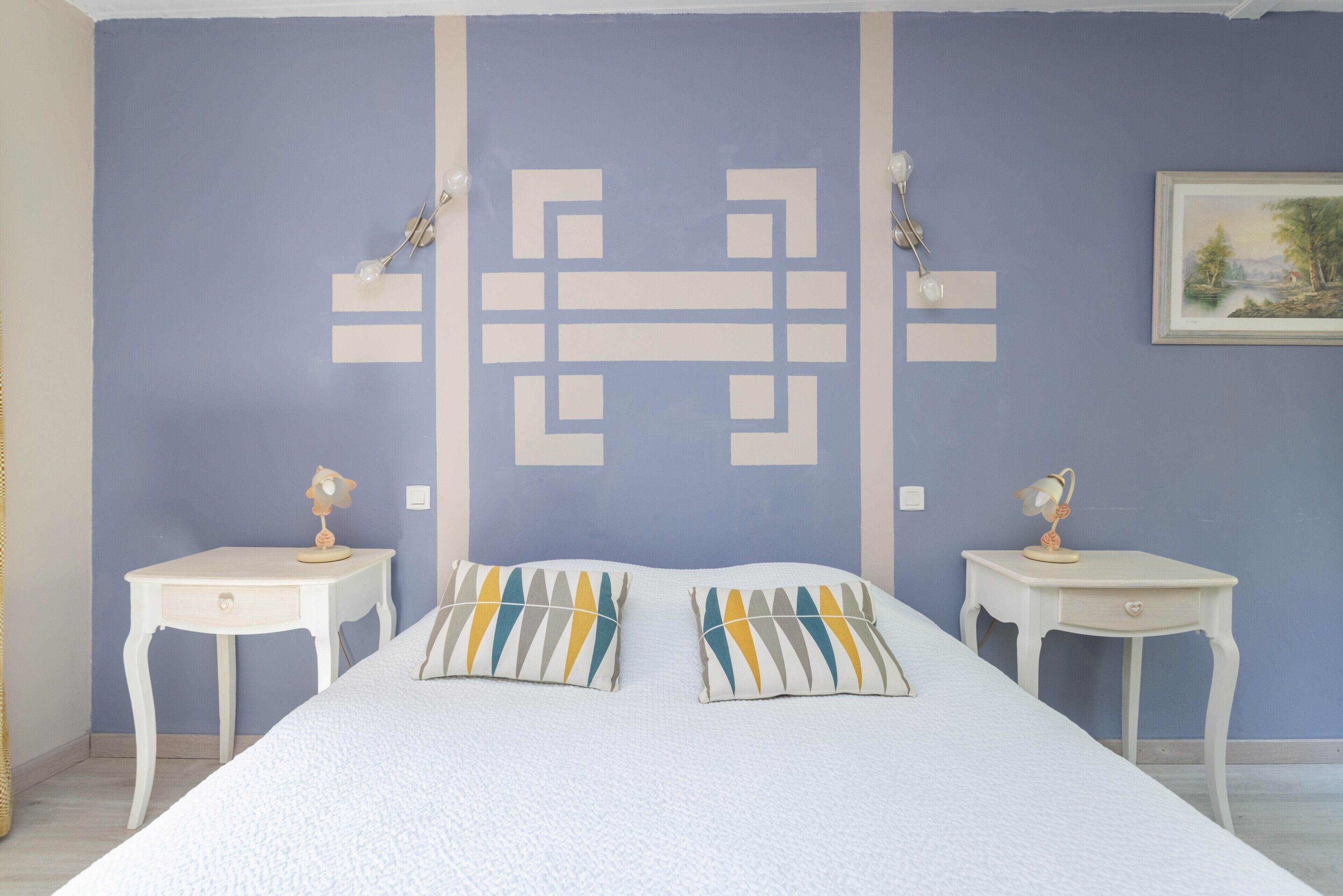 A bedroom with a bed, two bedside tables, and a wall with a geometric pattern.