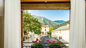 A balcony with a view of a narrow street, buildings, and mountains.