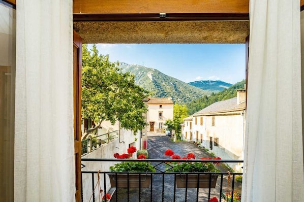 A balcony with a view of a narrow street, buildings, and mountains.