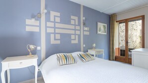A bedroom with a bed, a nightstand, a desk, a wall with geometric patterns, a picture, and a door leading to an outdoor area.