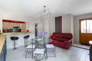 A modern kitchen with a dining area, a red leather sofa, and a glass table with chairs.