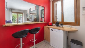 A compact kitchen with a red wall, a wooden countertop, a dishwasher, and two bar stools.