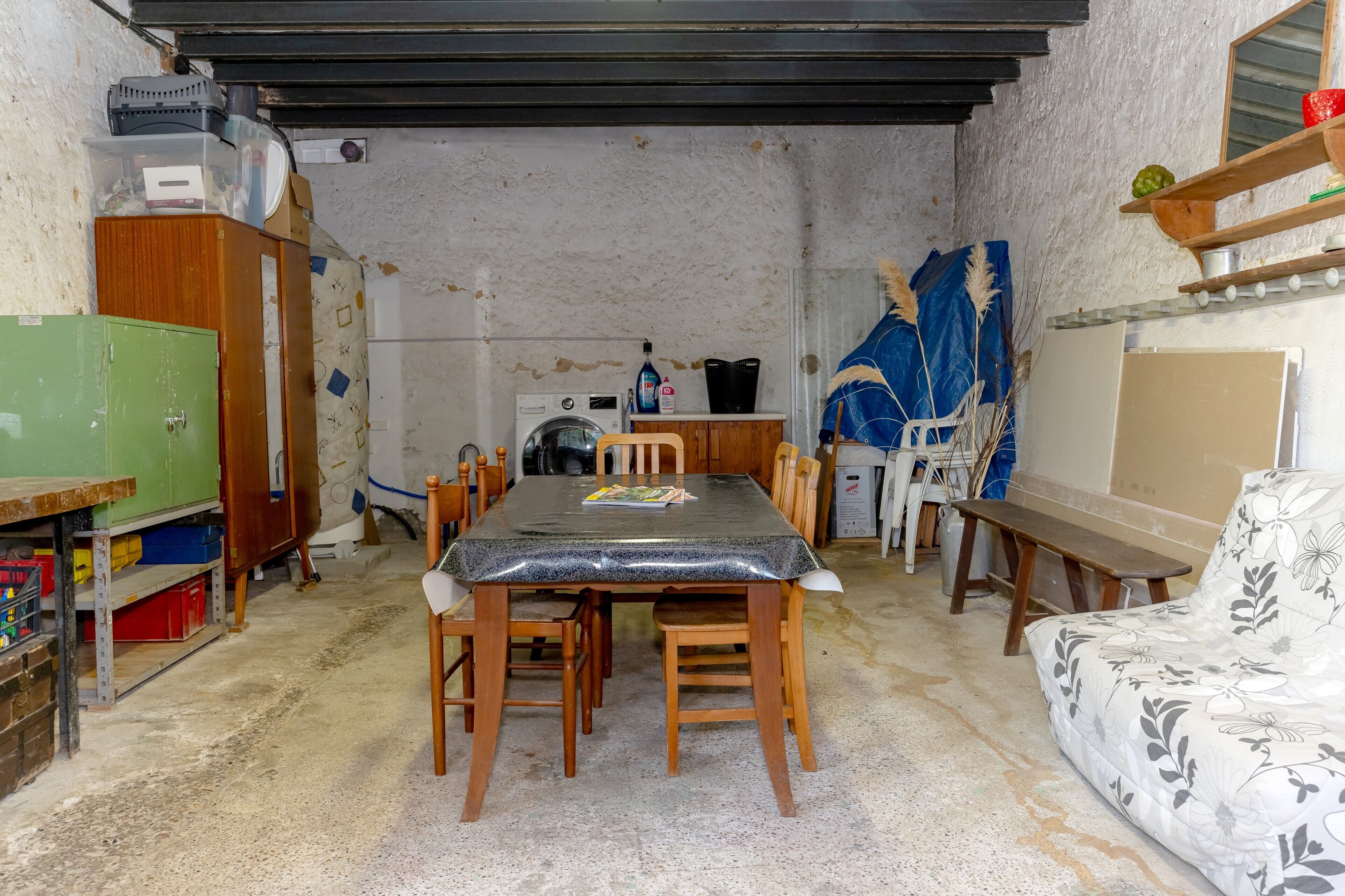 A compact room with a dining table, chairs, a sofa, a washing machine, and a small kitchen area.