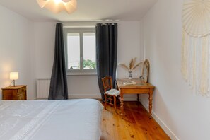 Ein Schlafzimmer mit Bett, einem Holztisch, einem Stuhl, einer Lampe, einem Fenster mit Vorhängen und einer Wanddekoration.