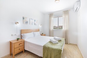 A hotel room with a bed, bedside tables, a nightstand, a window with curtains, and wall-mounted artwork.