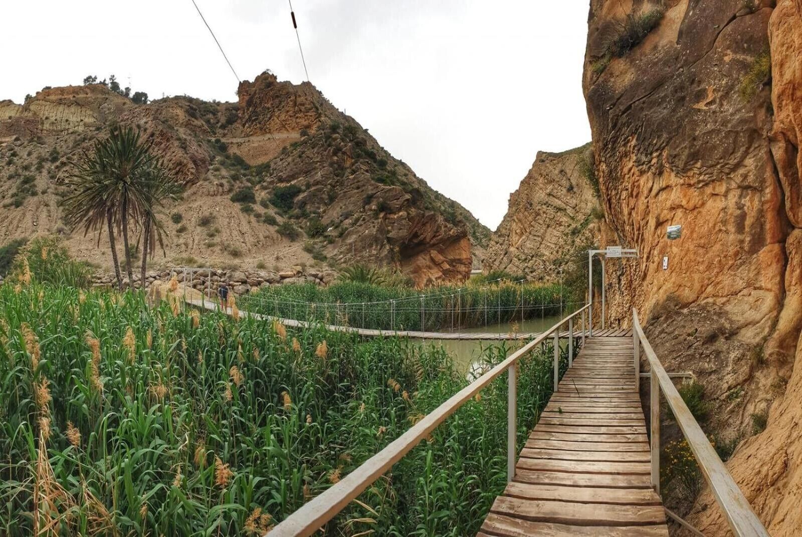 A wooden bridge leading to a rocky cliff with a signpost.