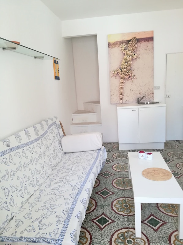 Una sala de estar con un sofá estampado, una mesa de centro, una zona de cocina con un lavabo y una escalera.