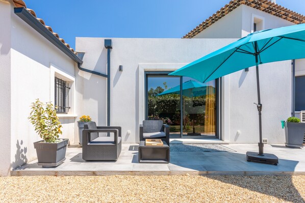 Un patio moderno con mobiliario exterior, un paraguas azul y una planta en maceta.