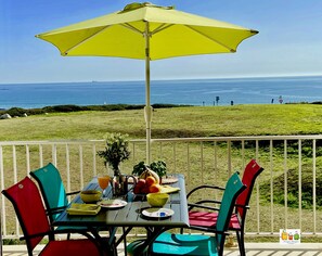 Una mesa con sillas y un paraguas amarillo en un balcón con vista al océano.